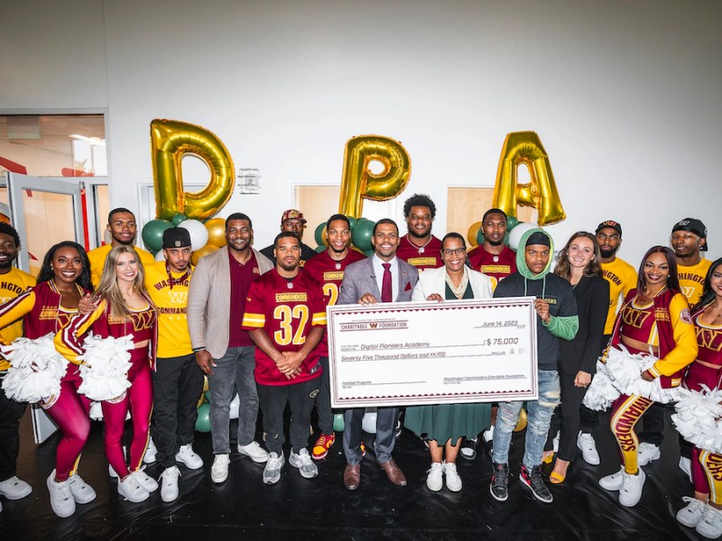 Washington Commanders President Jason Wright and Digital Pioneers Founder Mashea Ashton hold a check for a $75,000 donation from the team to start a football program at the school. (Courtesy of Washington Commanders Media Relations)