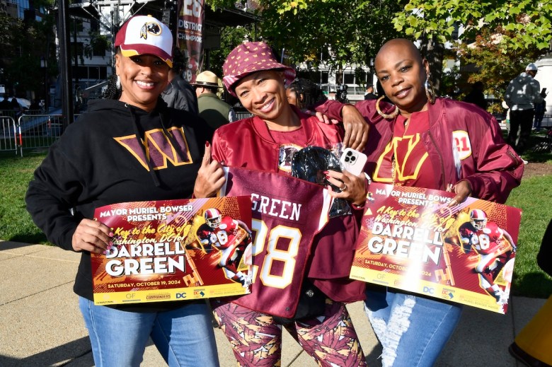 Washington fans Stacy Wills, Shenee Latimore and Mercedes Beverly hold up signs for Darrell Green on Saturday, Oct. 19. D.C. Mayor Muriel Bowser held a celebration honoring the legendary quarterback with a ceremonial key to the city. (Robert R. Roberts/The Washington Informer)