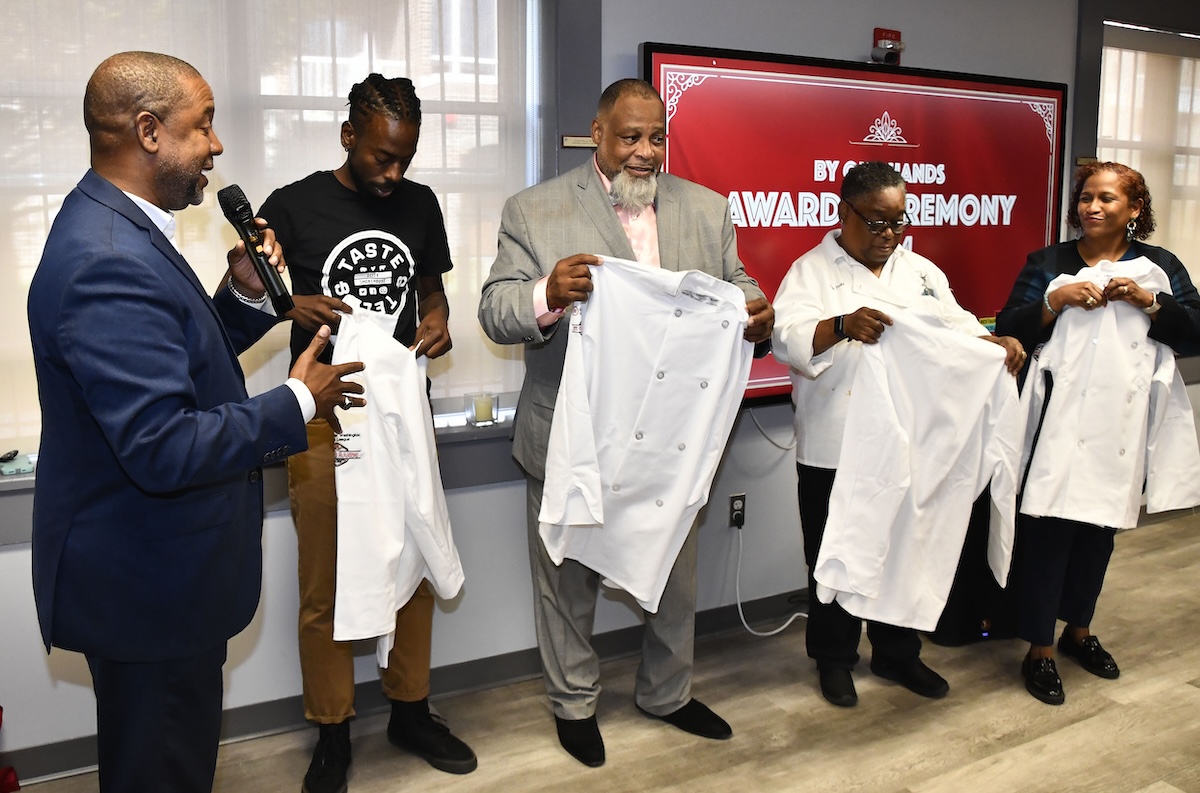 Furard Tate, executive director of entrepreneurship at the Greater Washington Urban League, awards Joseph McPherson, Reese Dixon, Leah Todd and Michelle Phipps with chef's tunics at the By Our Hands award ceremony on Sept. 21. (Robert R. Roberts/The Washington Informer)