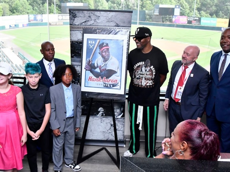 Dwayne Sims of the Negro League Legends Hall of Fame and Mark Wahl of the United States Postal Service, stand beside a blown-up image of the Hank Aaron stamp. (Robert R. Roberts/The Washington Informer)