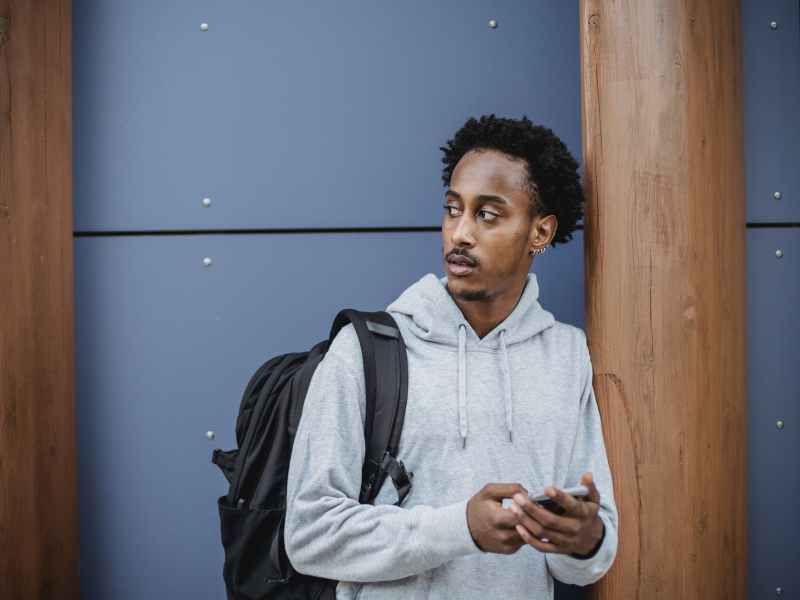 serious young black man browsing smartphone on street