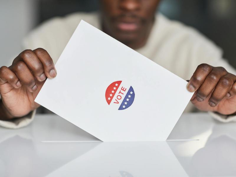 person putting a paper in white ballot box